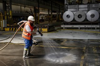 Deux employes de Novelis Sierre nettoient la boue entre les machines sur le site du fabriquant d'aluminium Novelis le jeudi 11 juillet 2024 a Sierre. Les entreprises Constellium et Novelis, devastees par le debordement du Rhone le week-end dernier, ont tenu jeudi une conférence de presse commune avec l'Etat du Valais. Ils reclament des mesures de protection urgentes. (KEYSTONE/Jean-Christophe Bott)